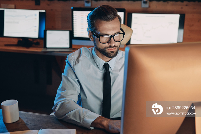 Concentrated young man working on computer while staying late in the office