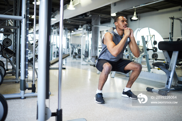 Guy in sportswear doing squats on the floor while training hard in gym or fitness center