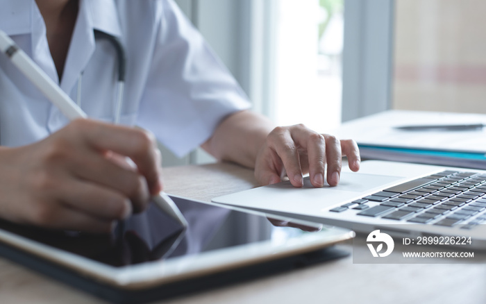 Female doctor working on digital tablet for health record and laptop computer in medical office