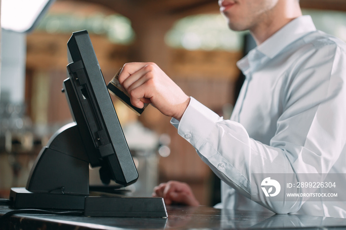 small business, people and service concept - happy man or waiter in apron at counter with cashbox working at bar or coffee shop.