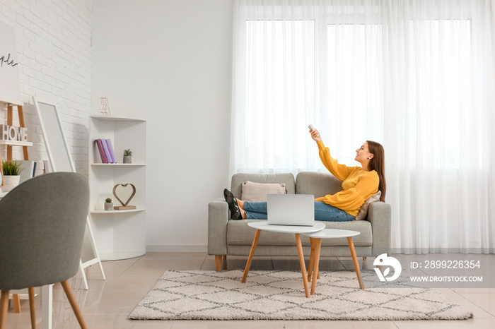 Young woman switching on air conditioner at home