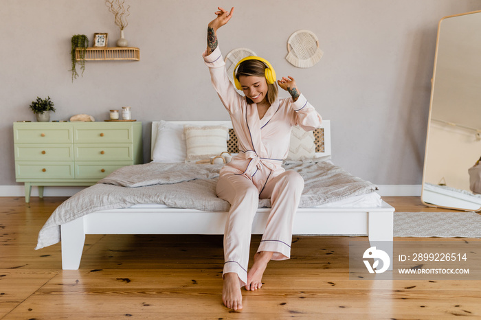 smiling woman relaxing at home on bed in morning in pajamas listening to music