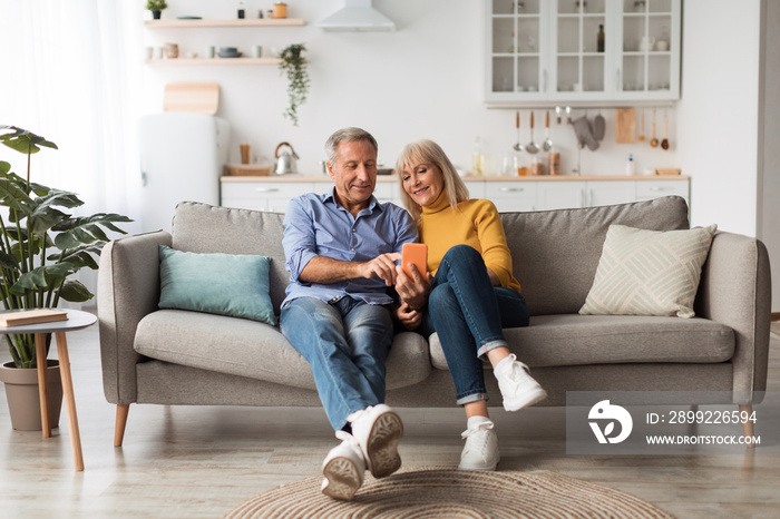 Happy Mature Husband And Wife Using Smartphone Sitting At Home