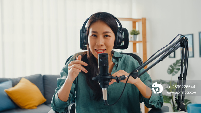 Happy asia girl record a podcast with headphones and microphone look at camera  talk and take a rest in her room. Female podcaster make audio podcast from her home studio, Stay at house concept.