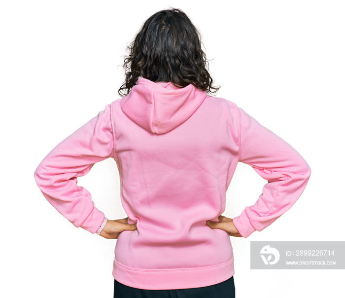 Young hispanic woman wearing casual sweatshirt standing backwards looking away with arms on body