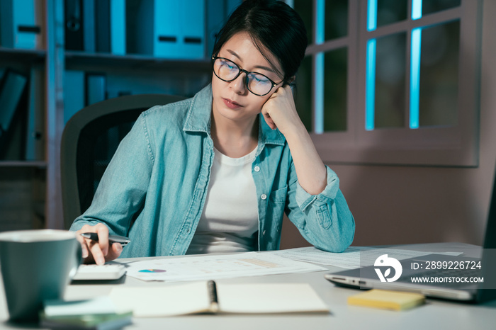 Close up of woman freelance worker using calculator while going through company finances in dark night. young girl designer working in home office counting numbers of architecture by window midnight