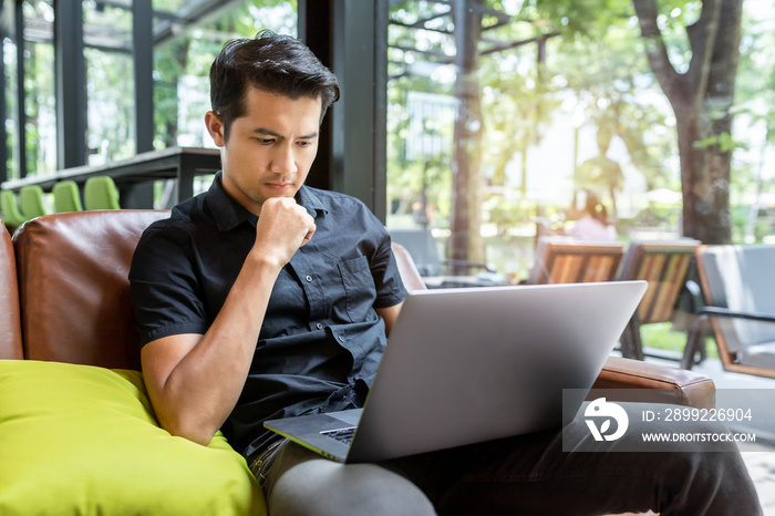 Asian man using gadgets Inspired, Confident young man working on laptop while sitting at his working place in coffee shop, Freelance work concept.