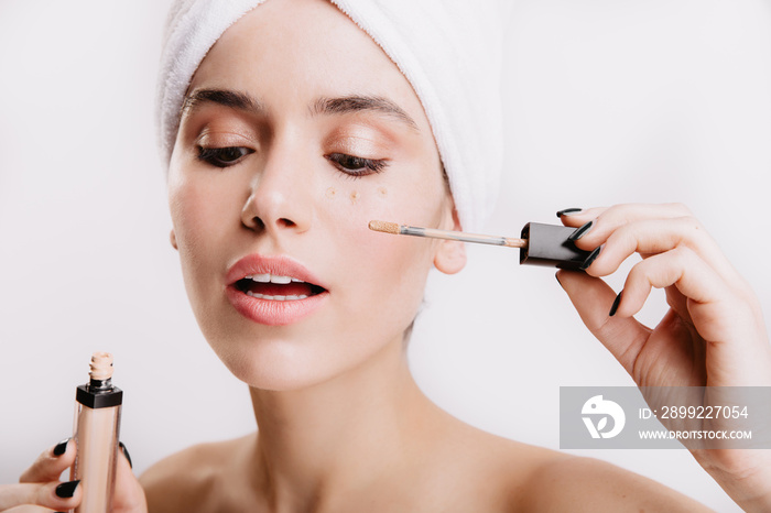 Beautiful girl after shower posing on white background. Woman puts concealer to hide bruises under eyes