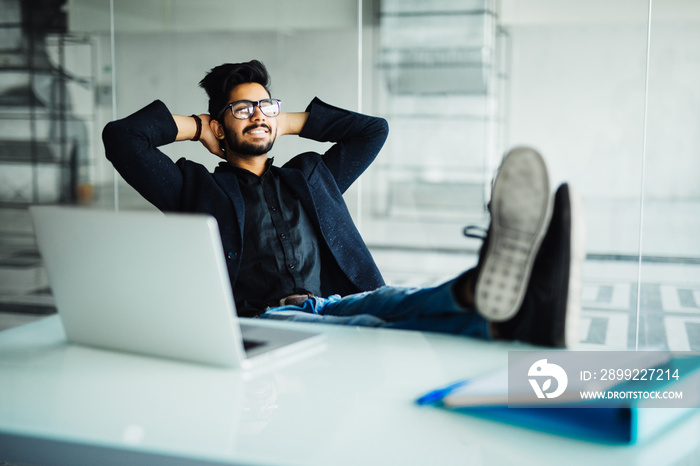 Young indian Businessman working in his office with feet on desk