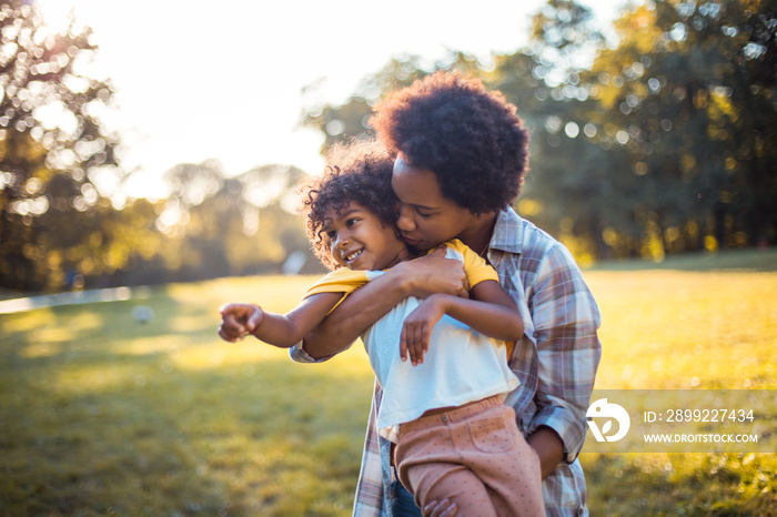 Mother holding her daughter and kissing.  African American mother and daughter standing in park.