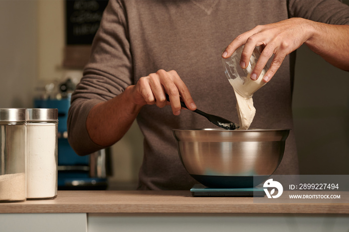 unrecognizable man pouring sourdough into a metal bowl on a digital scale