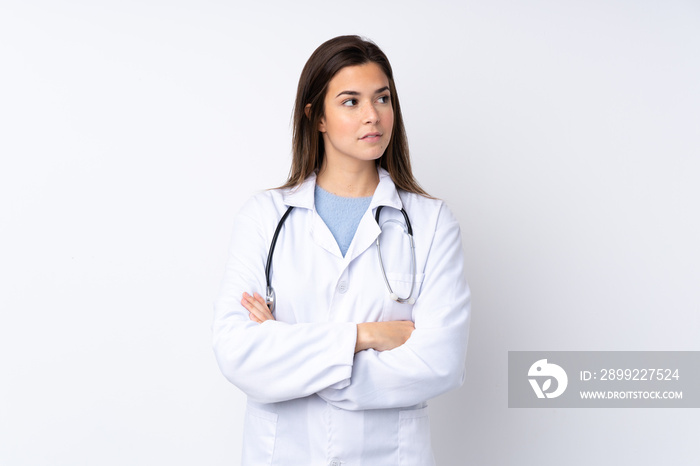 Teenager girl over isolated white background wearing a doctor gown and with arms crossed looking side