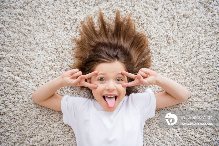 Photo of adorable funny small schoolgirl dressed white t-shirt stick out v-signs cover eyes indoors room home house