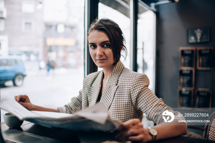 Serious woman with newspaper resting in cafe