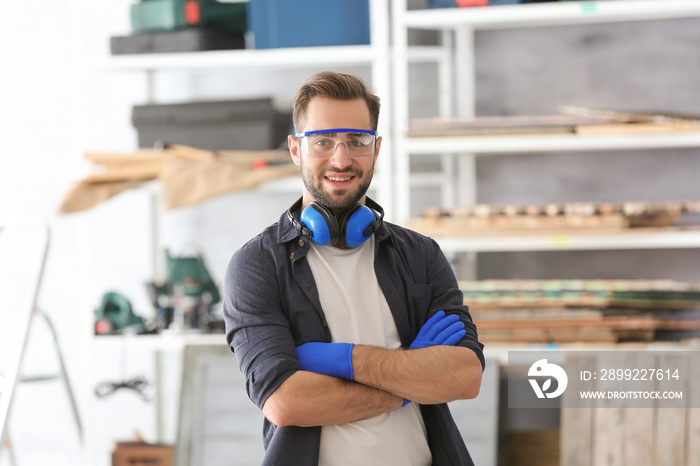 Young smiling carpenter standing with crossed hands in workshop