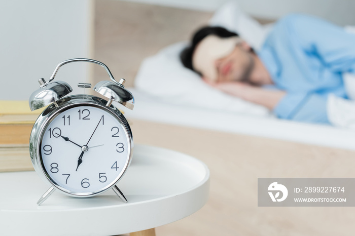 selective focus of vintage alarm clock near man sleeping on blurred background.