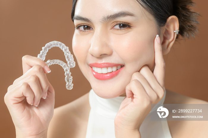 A young woman with beautiful teeth is holding Invisalign, healthy dental concept