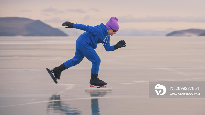 The child train on ice professional speed skating. The girl skates in the winter in sportswear, sport glasses, suit. Children speed skating short long track, kid sport. Outdoor slow motion.