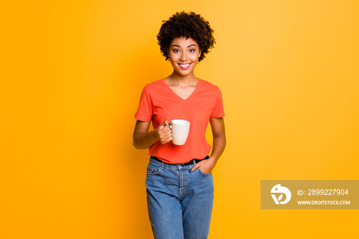 Photo of attractive cheerful cute nice charming trendy black girlfriend wearing denim jeans holding cup of coffee while isolated over yellow vivid color background