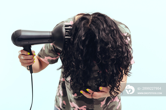 Woman makes herself curly hairstyle. Girl using a modern hairdryer.