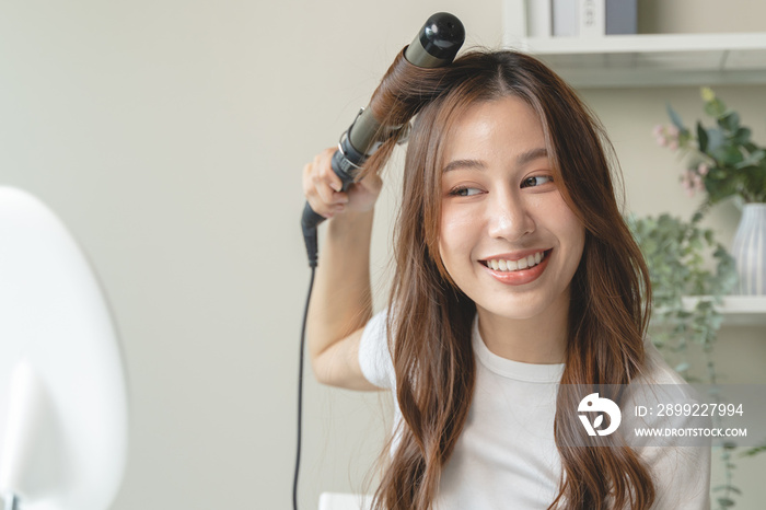 women hairdo makeup routine, Young woman looking at the mirror and using iron hair curling curly long hair at home.