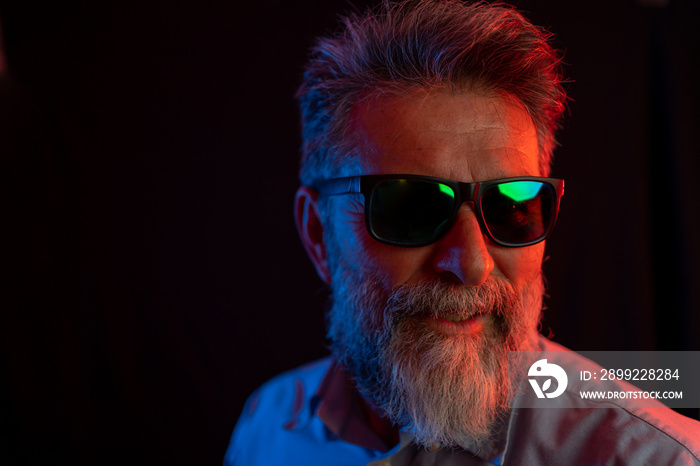 Neon light studio close-up portrait of serious man model with mustaches and beard in sunglasses