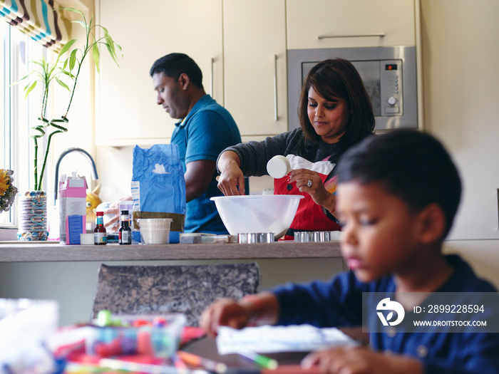 Boy drawing at table while parents cooking