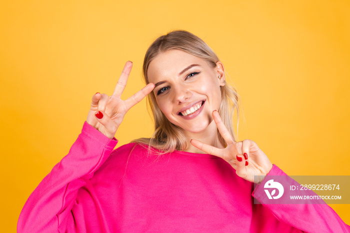 Pretty european woman in pink blouse on yellow background happy cheerful positive smile doing victory gesture