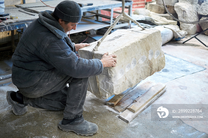 Sculptor gem-worker lifts a crane a piece of marble.