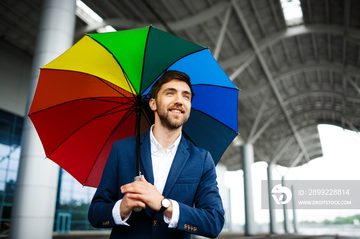 Picture of  cheerful young businessman holding motley umbrella  in the street