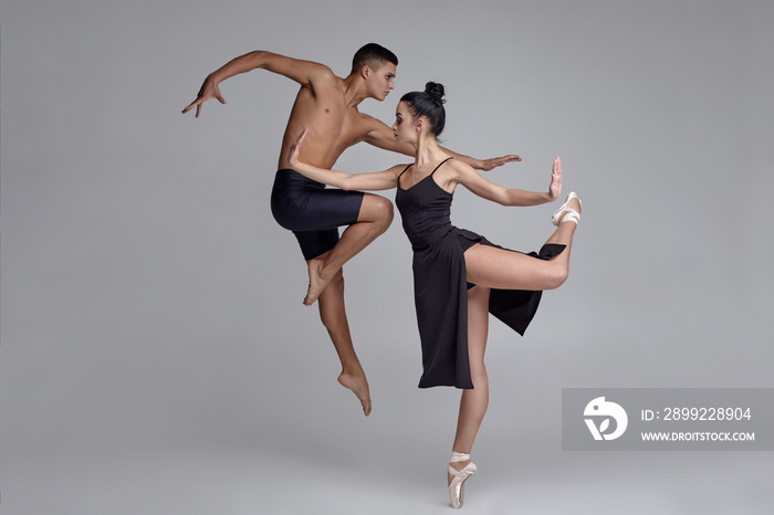 Two athletic modern ballet dancers are posing against a gray studio background.