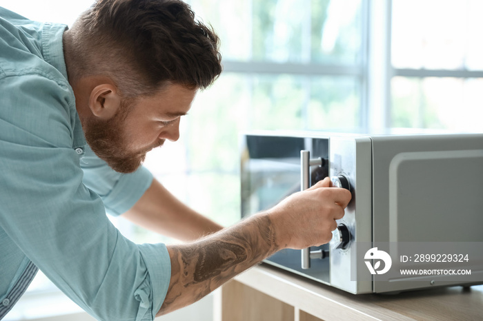 Young man adjusting microwave oven in kitchen