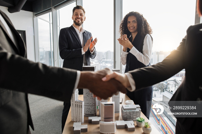 Selective focus on two business people applauding and their colleagues businesspeople real estate, agents developers handshake after successful deal, city district urban planning project good work.