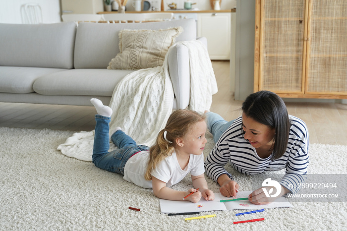 Little daughter and mother drawing painting lying together on floor. Educational pastime, creativity