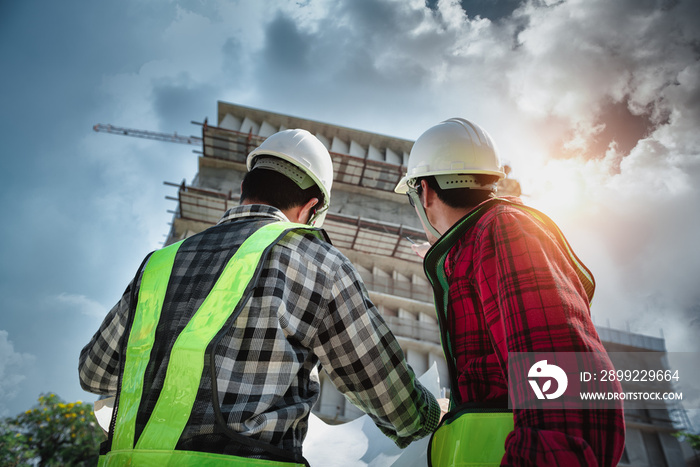 Construction engineers discussion with architects at construction site or building site of highrise building with blueprints.