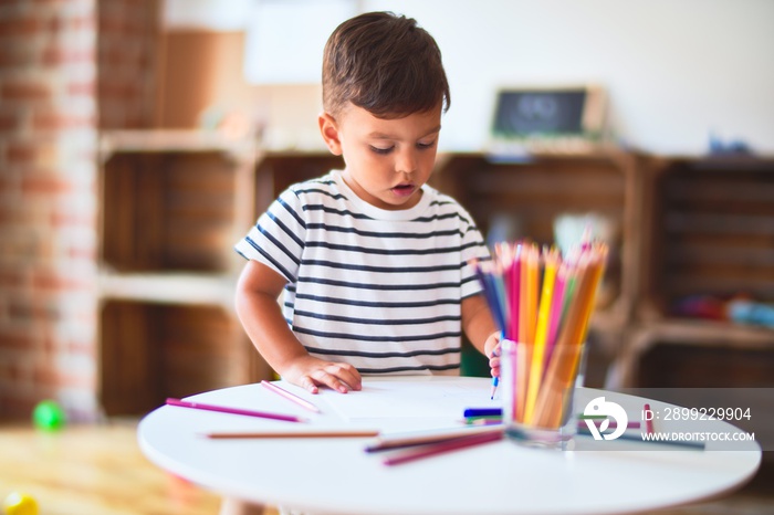 Beautiful toddler boy drawing cute draw using colored pencils at kindergarten