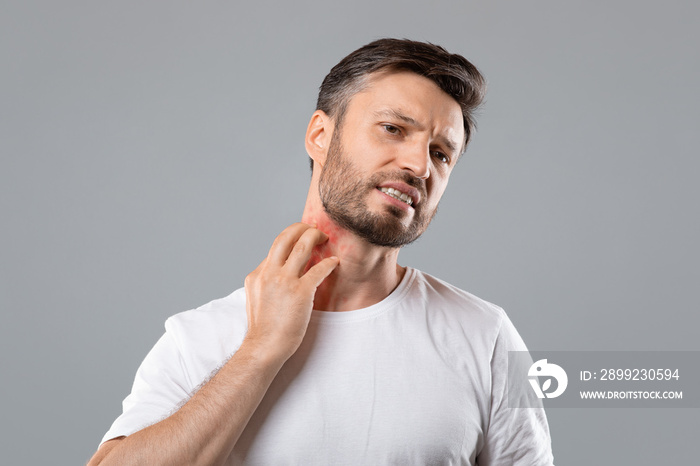 Bearded man scratching neck on grey background, having annoying itch