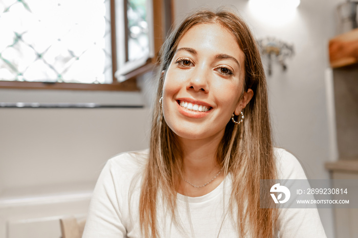 Confident young beautiful woman smiling looking at the camera for a video call conference in her home - Portrait of a cute long hair female alone person at home - New normal social communication