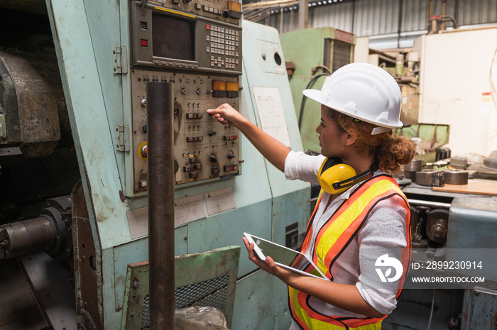 Female industrial worker working and checking machine in a large industrial factory with many equipment.