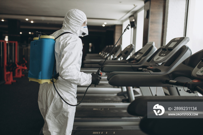 Cleaning and Disinfection in crowded places amid the coronavirus epidemic Gym cleaning and disinfection Infection prevention and control of epidemic. Protective suit and mask and spray bag