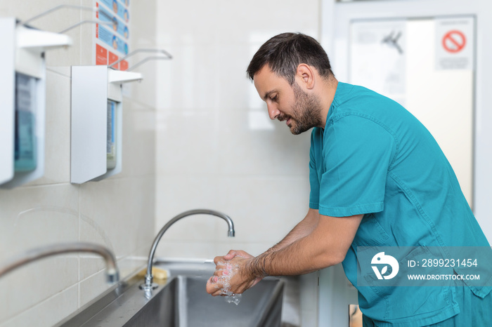 Doctor washing hands with soap. Male surgeon is preparing for surgery. He is in uniform at operating room.