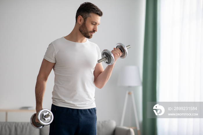 Closeup of handsome bearded man doing dumbbell workout at home