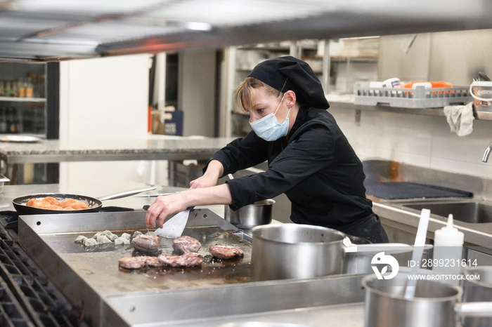 Woman Chef in protective face mask prepare food in the kitchen of a restaurant or hotel. Coronavirus prevention concept. High quality photo