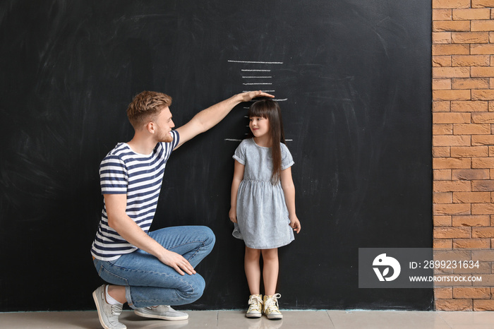 Father measuring height of his little daughter near wall with marks