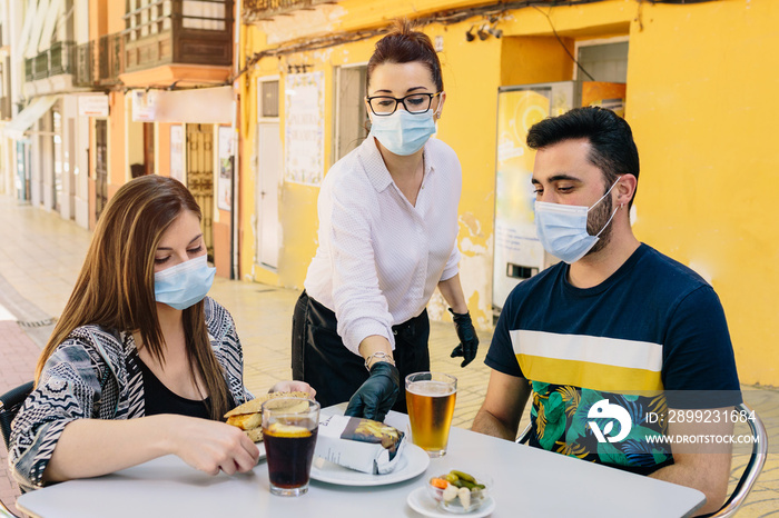 Clients with masks on the terrace of a bar in Spain attended by a waiter with gloves and masks. Social distancing during phase one of de-escalation. Coronavirus