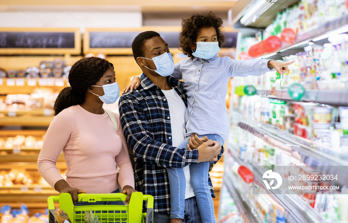 Family shopping during coronavirus pandemic. Black family with child wearing face masks, purchasing food at supermarket