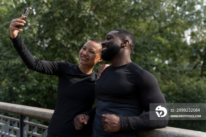 Smiling athletic man and woman taking selfie in park