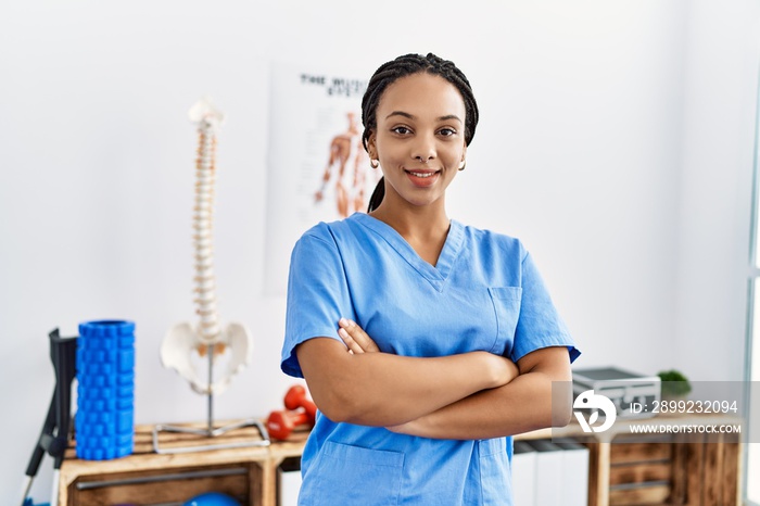 Young african american woman wearing physio therapist uniform standing with arms crossed gesture at clinic