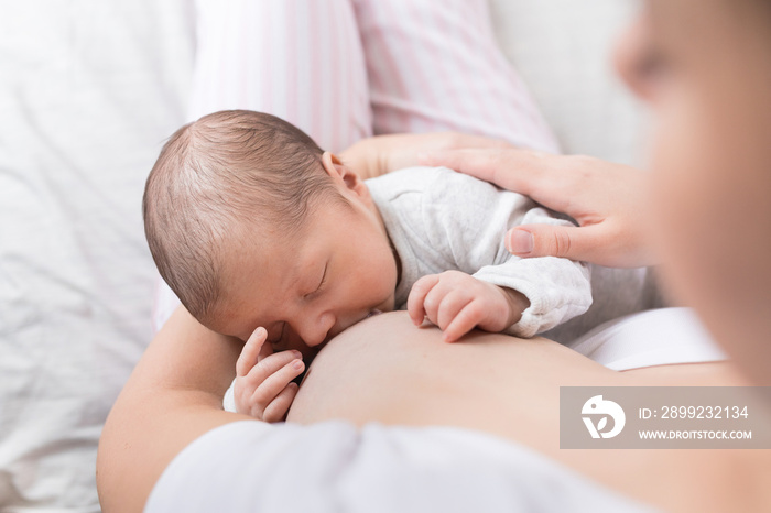 A young mother breastfeeding her newborn baby boy while holding in her arms at bedroom at home.