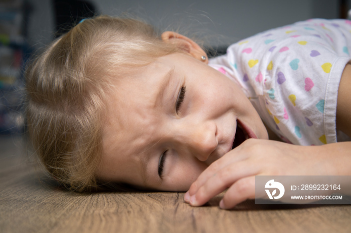 Frightened screaming child girl in t-shirt lying on wooden floor.